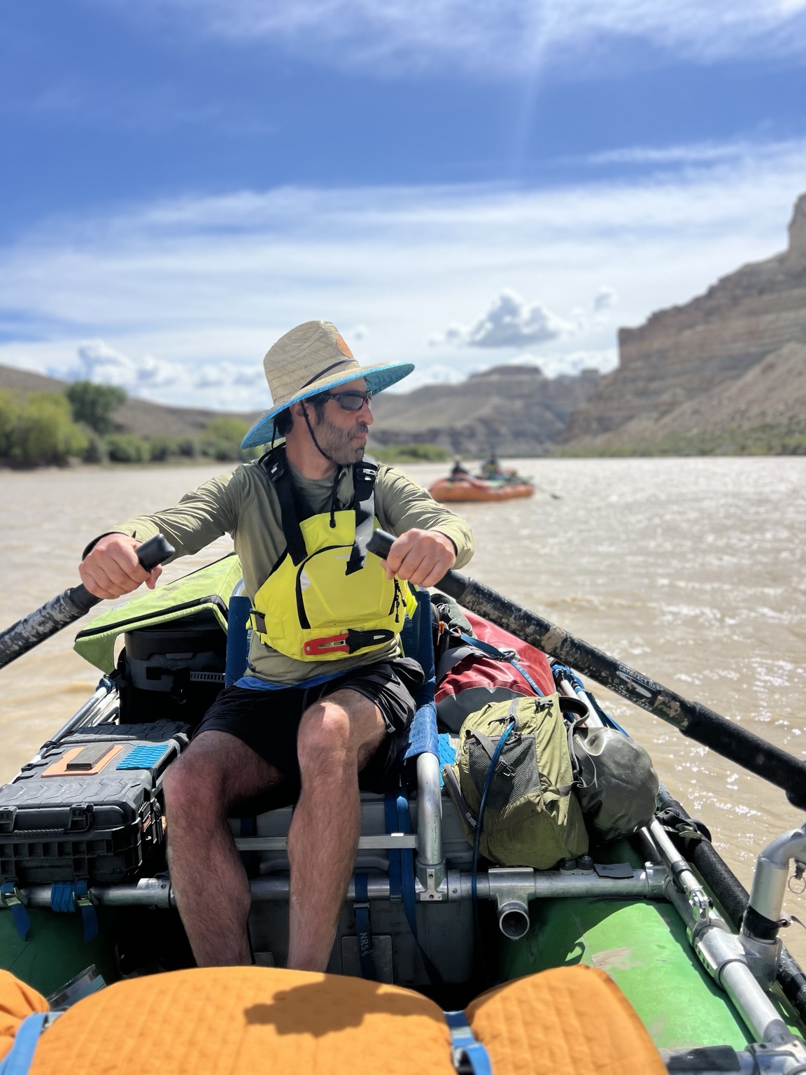 Adam Aronovitz rowing a raft through a river canyon with another raft in the distance.